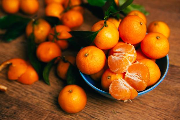 many fresh mandarin oranges in  blue bowl, standing on a wooden table 