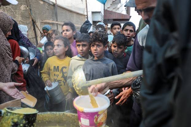 Palestinians gather to receive meals cooked by a charity kitchen, in Deir Al-Balah, central Gaza Strip