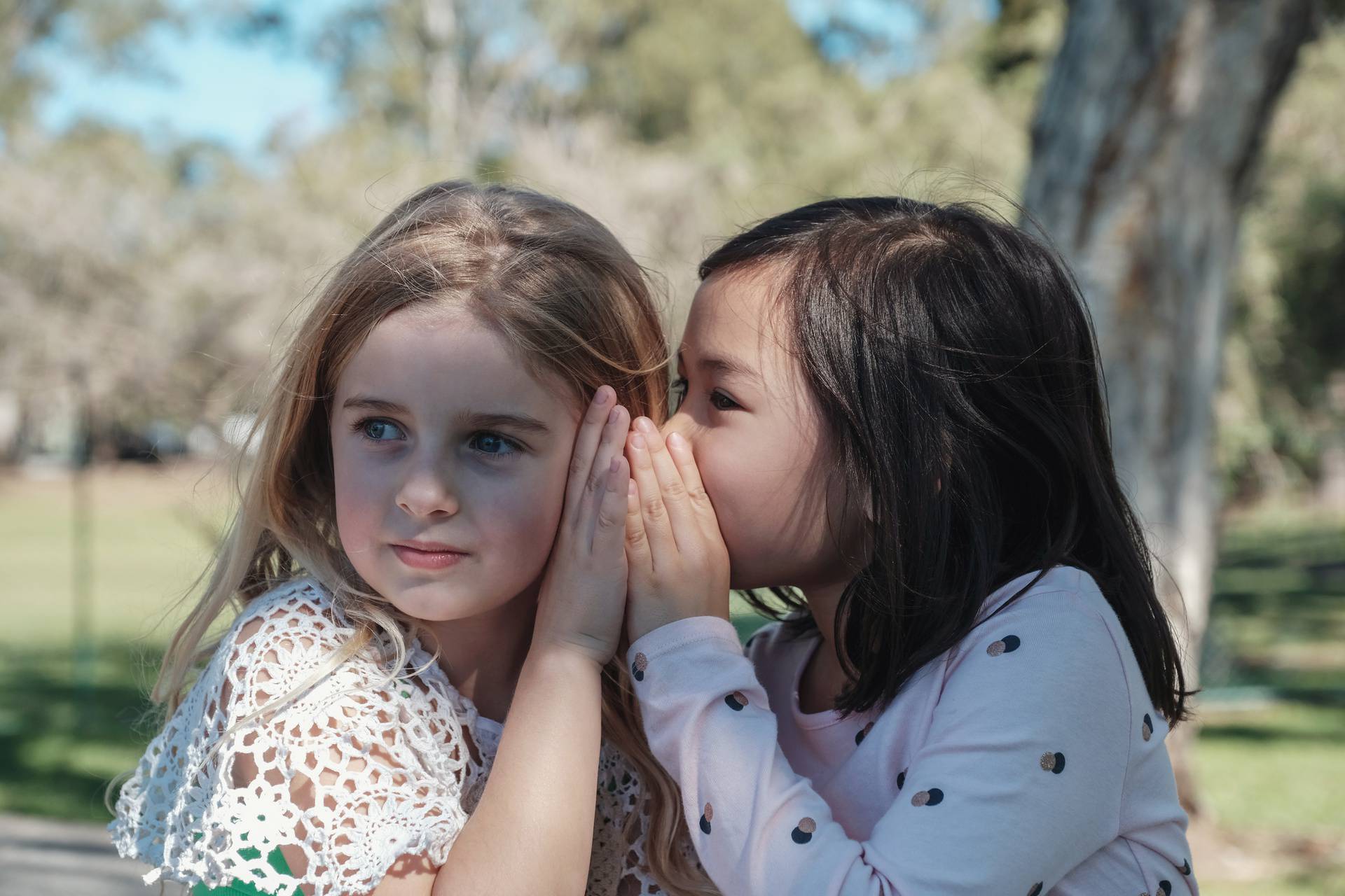 Mixed ethnic young little girls playing Chinese whispering  in t