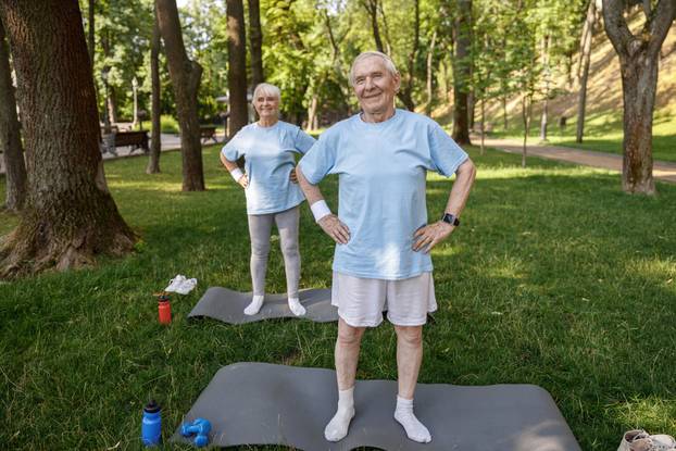 Sportive mature man and woman train on mats on lush lawn