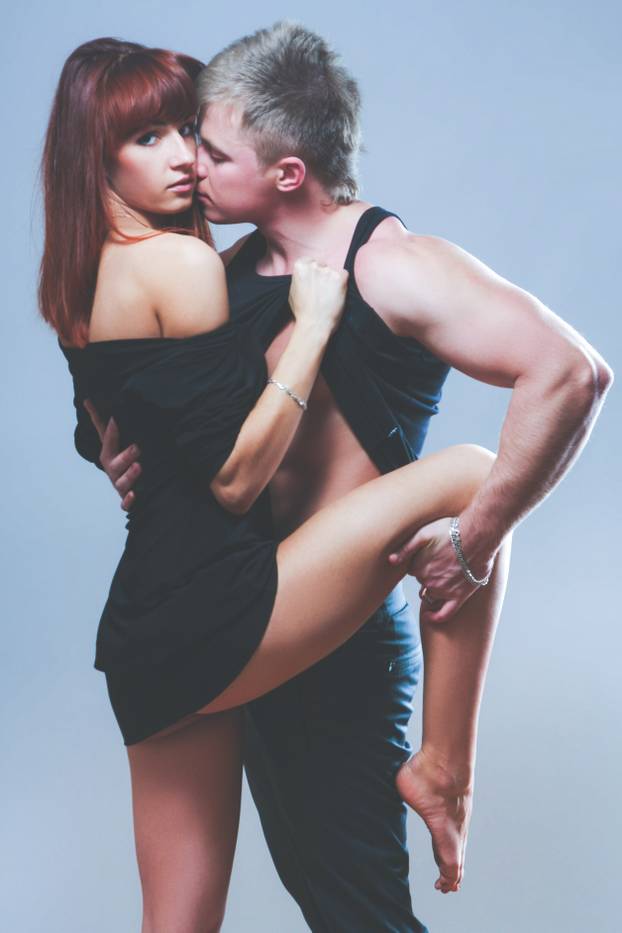 Embracing glamorous couple standing on dark background