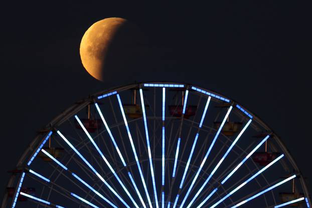 A lunar eclipse of a full "Blue Moon" is seen above the ferris wheel on the Santa Monica Pier in Santa Monica