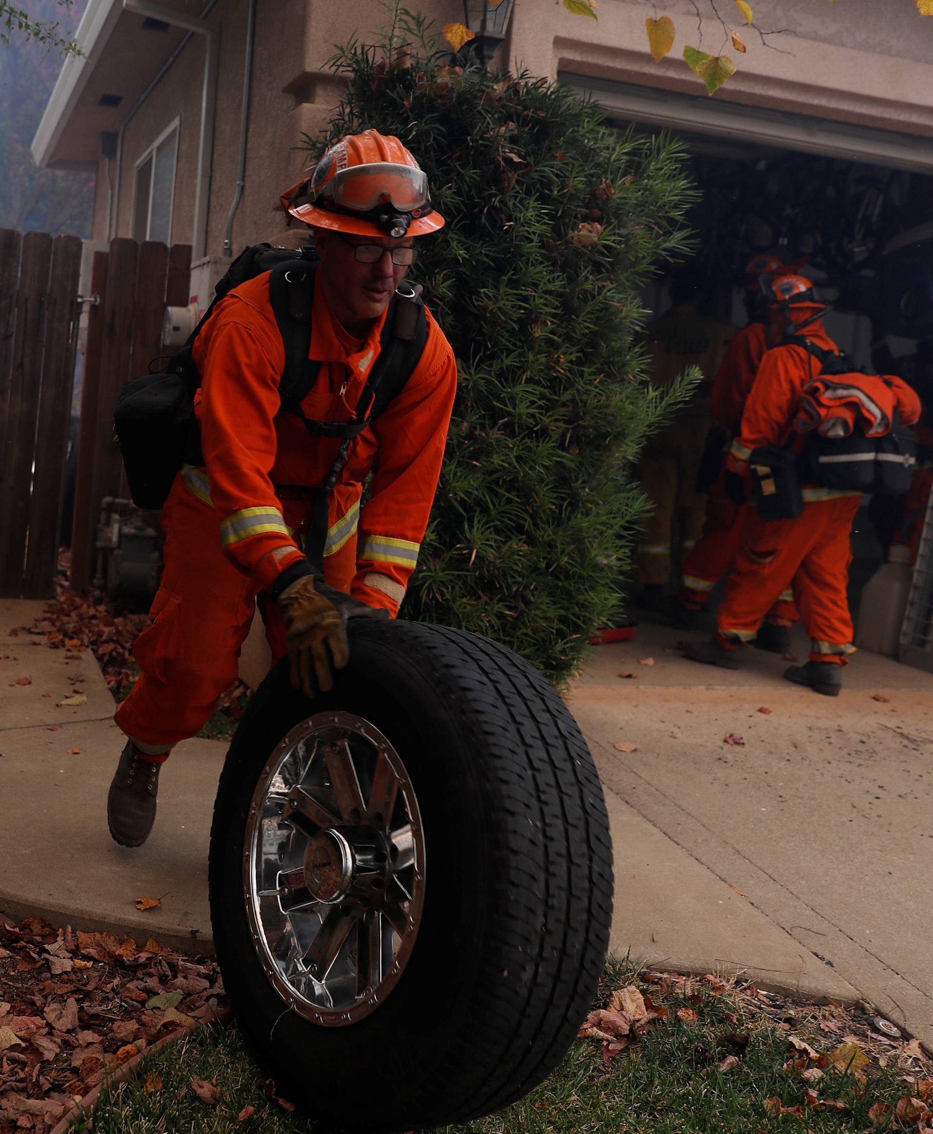 Inmate firefighter removes a wheel from a burning home while battling the Camp Fire in Paradise