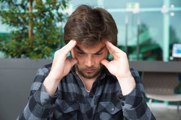 Thoughtful man touching temples and thinking in street cafe