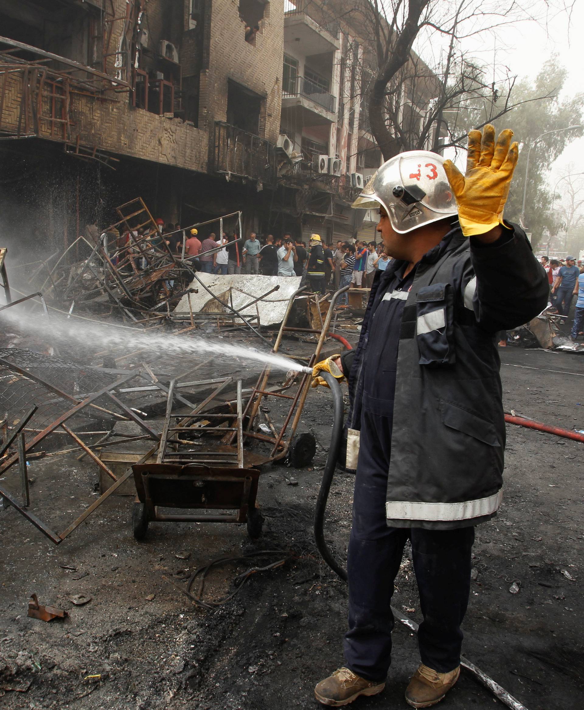 Firemen hose down a burning building as civilians gather after a suicide car bomb occurred in the Karrada shopping area in Baghdad, Iraq