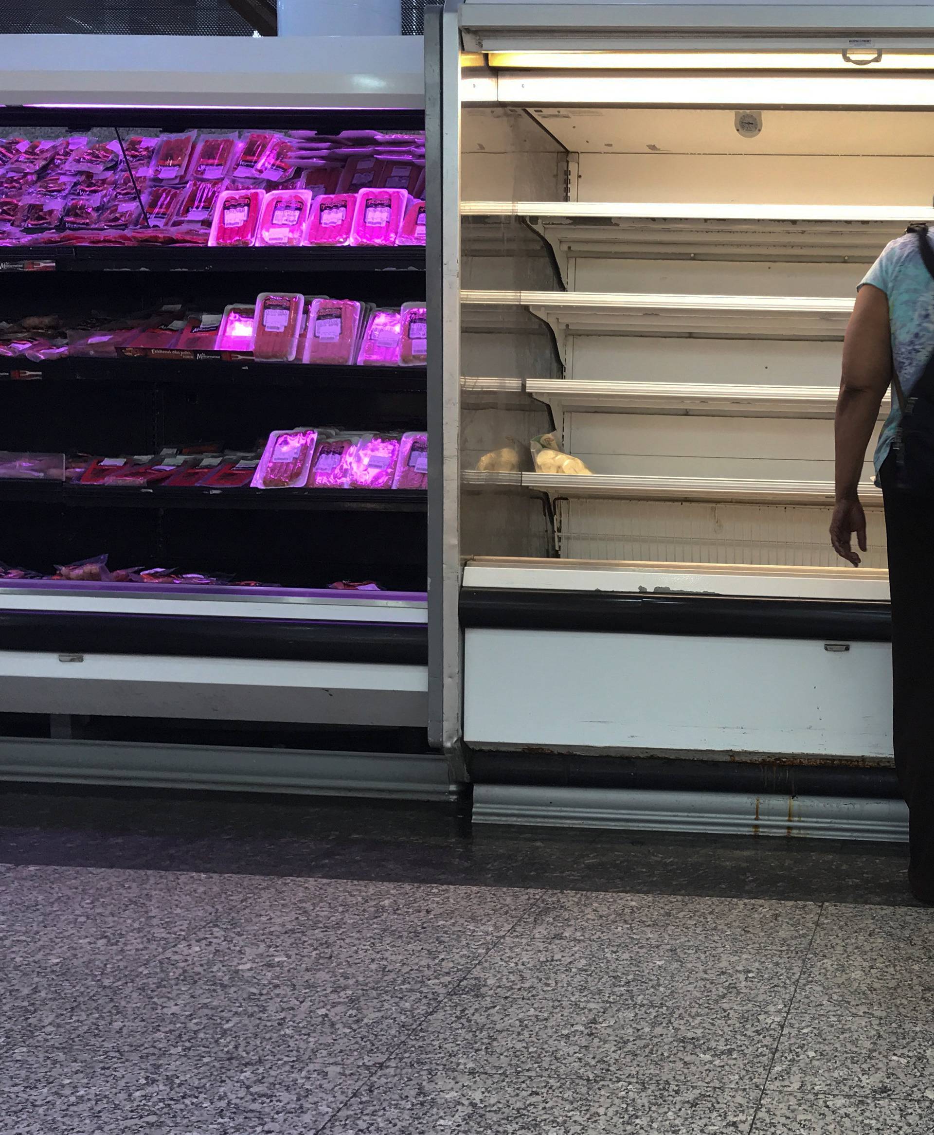 A woman stands in front partially of empty refrigerators at a supermarket in Caracas
