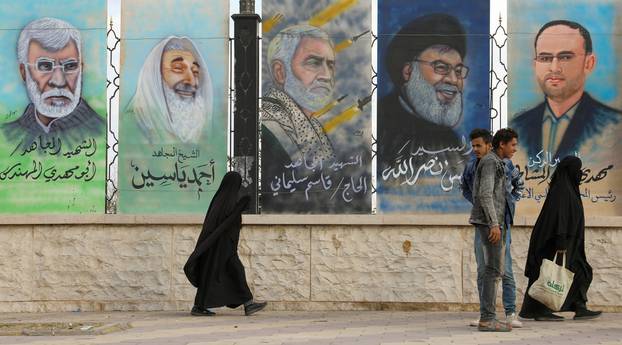 People walk past posters of Abu Mahdi al-Muhandis, Ahmad Yassin, Qassem Suleimani, Sayyed Hassan Nasrallah and Mahdi al-Mashat in Sanaa