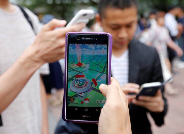 Men play the augmented reality mobile game "Pokemon Go" by Nintendo on their mobile phone near a busy crossing in Shibuya district in Tokyo
