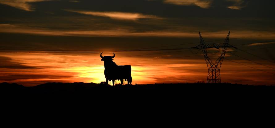 Power lines connecting pylons of high-tension electricity and a billboard-sized figure of a bull, known as the "Osborne bull", are seen at sunset in El Berron