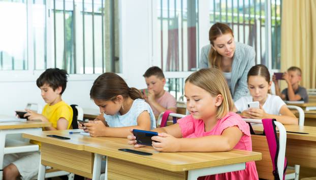 Absorbed preteen school children using mobile phones at lesson