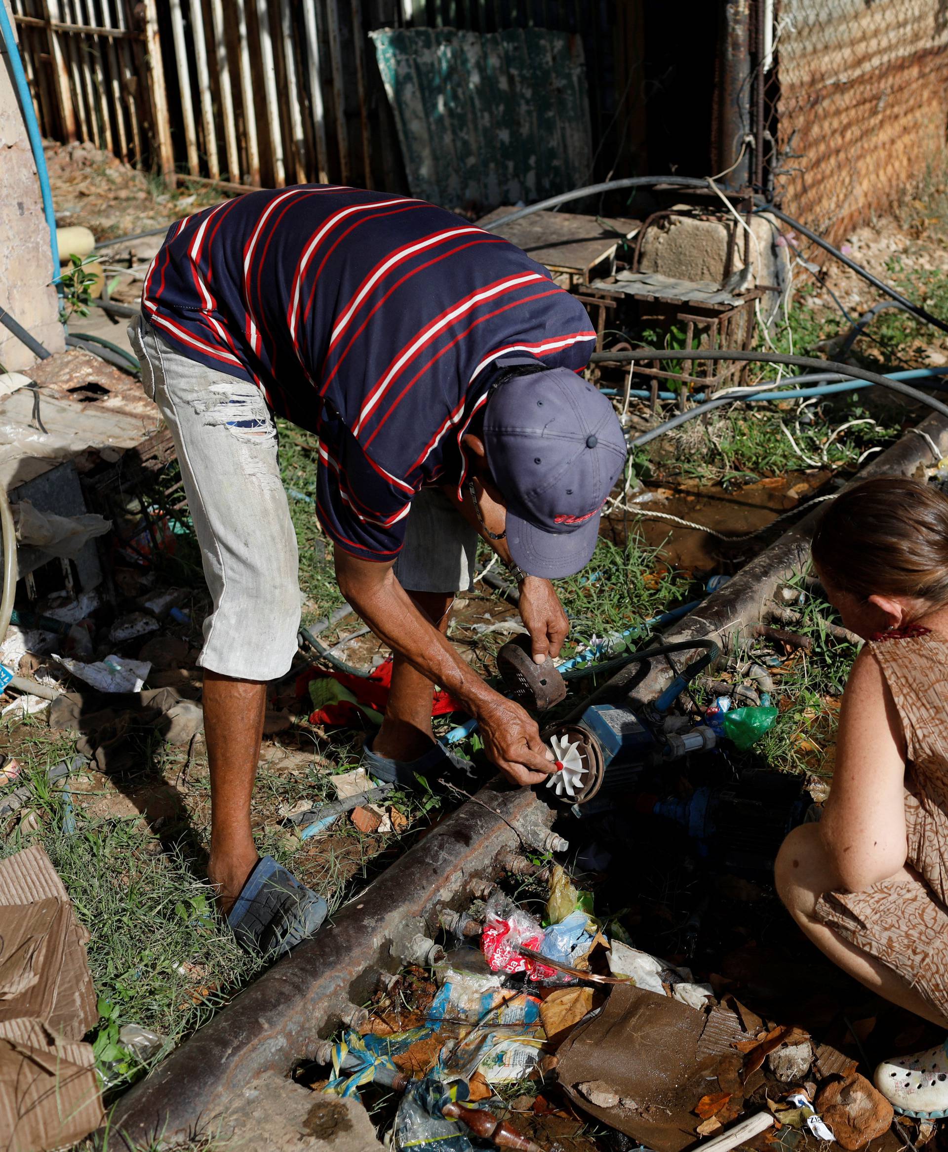 People set up a pump and fill buckets with water from a pipe in a street of Maracaibo