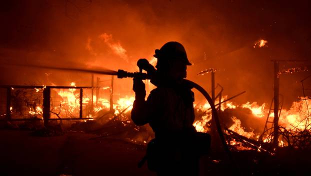A firefighter hoses down a property engulfed in flames during the Woolsey Fire in Malibu