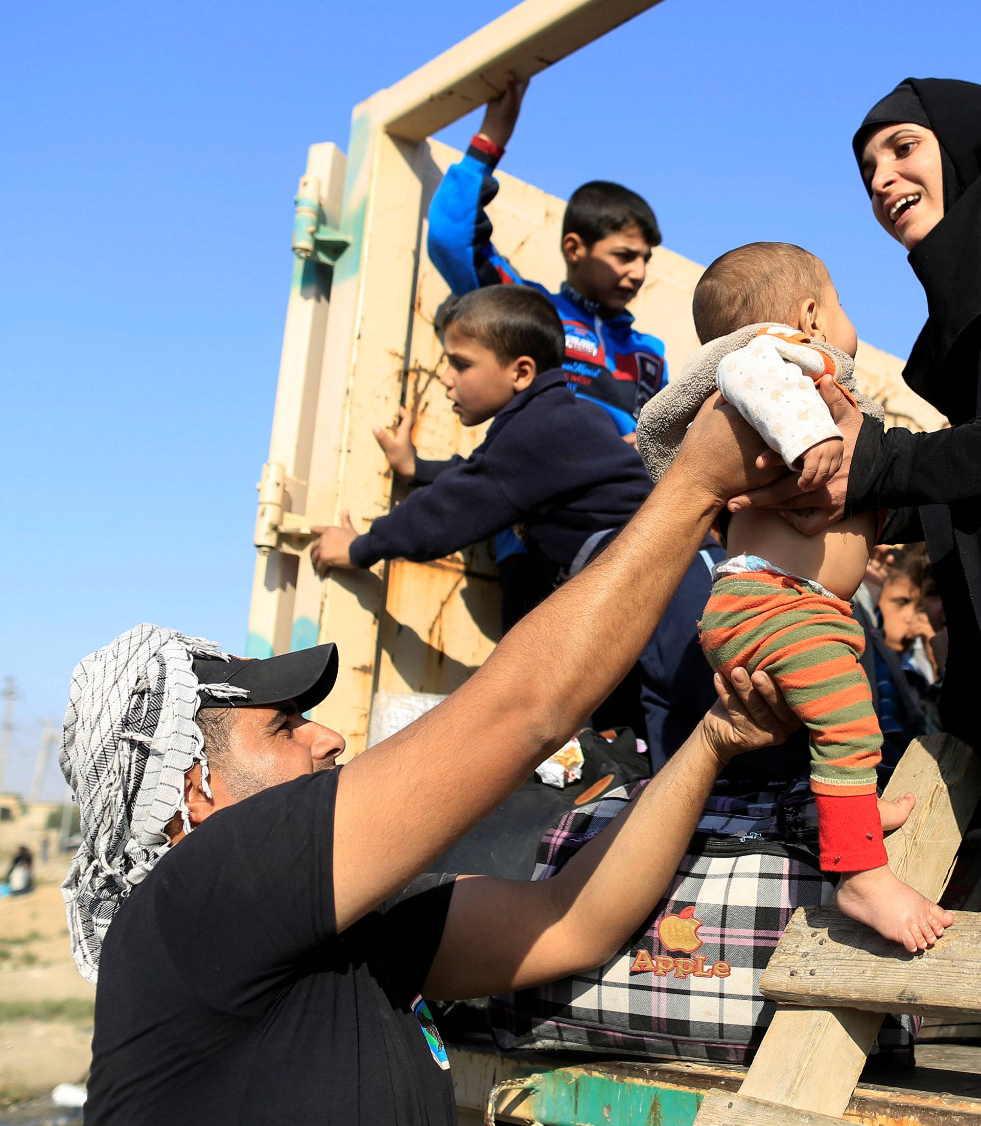 A soldier hands a baby to the mother, who had just fled the Samah district of eastern Mosul, on board a military truck at the Iraqi Special Forces checkpoint in Kokjali