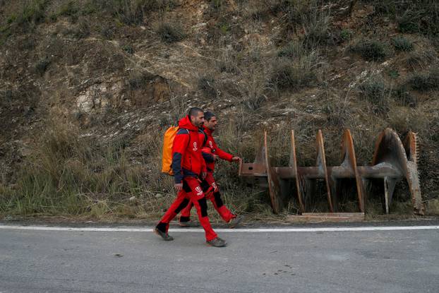 Mountain rescue firefighters walk past a piece of a drill on a road in Totalan