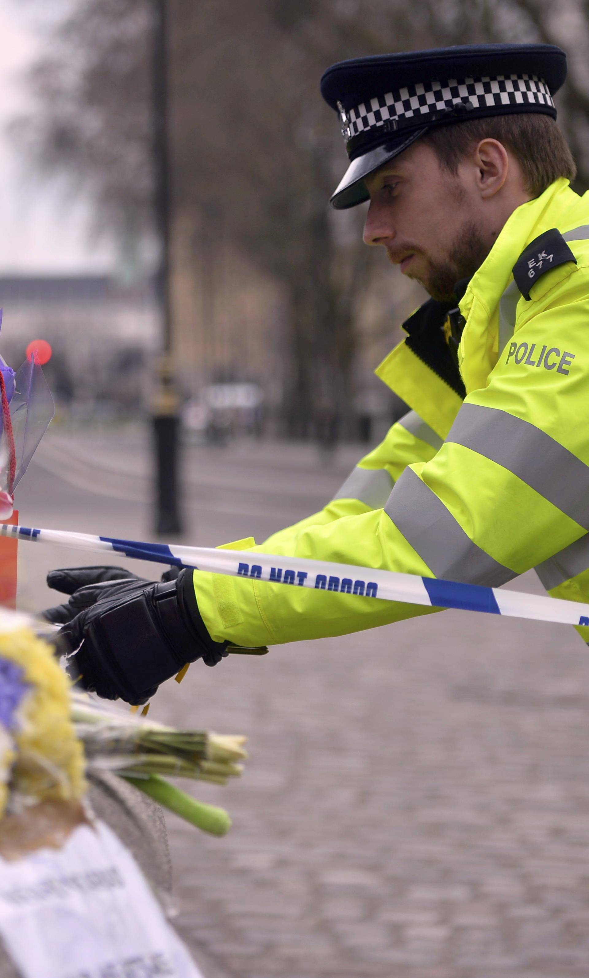 A police officer reaches out to floral tributes in Westminster the day after an attack, in London