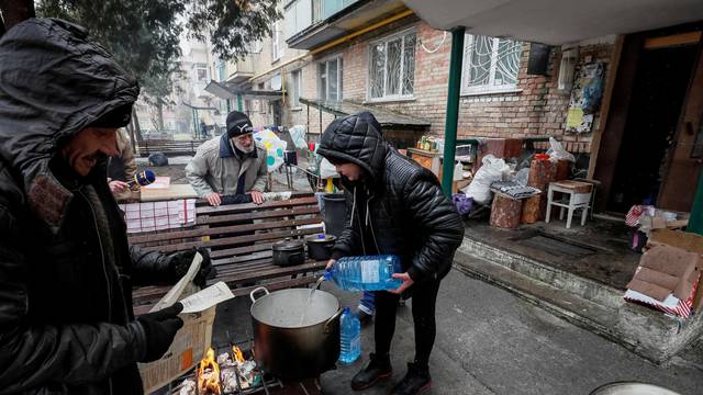 Locals residents cook food on a fire in the yard of their house in Bucha