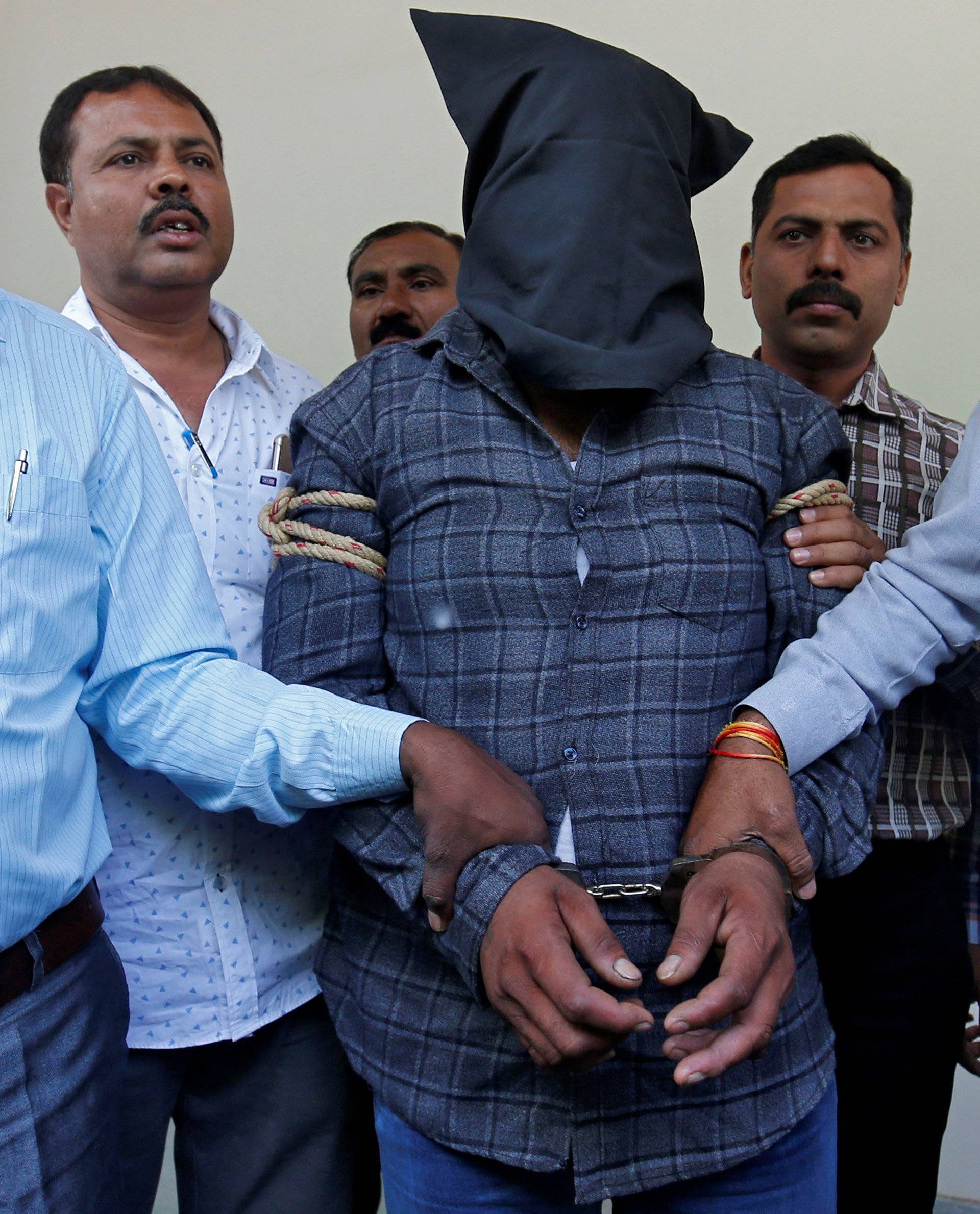 Plain-clothes police officers escort Harshsai Gurjar, who is accused of sexual attack and murder of an 11-year-old girl, to present him before the media at a crime branch office in Ahmedabad