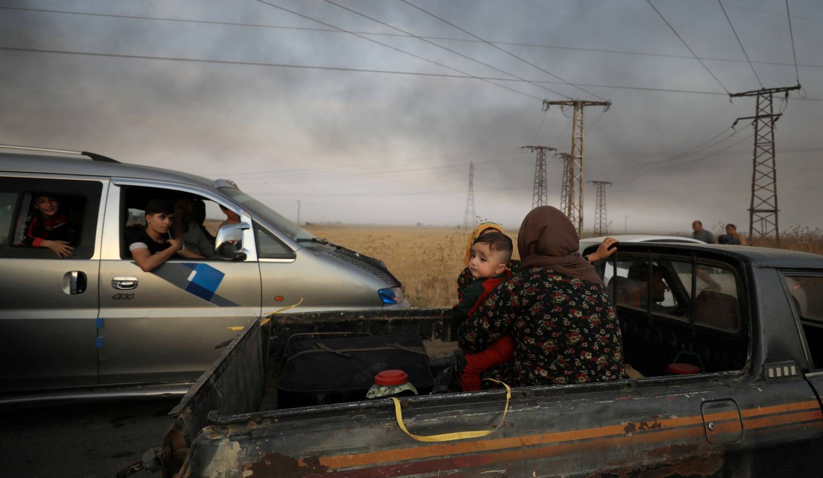 A woman with a baby sits at a back of a truck as they flee Ras al Ain town