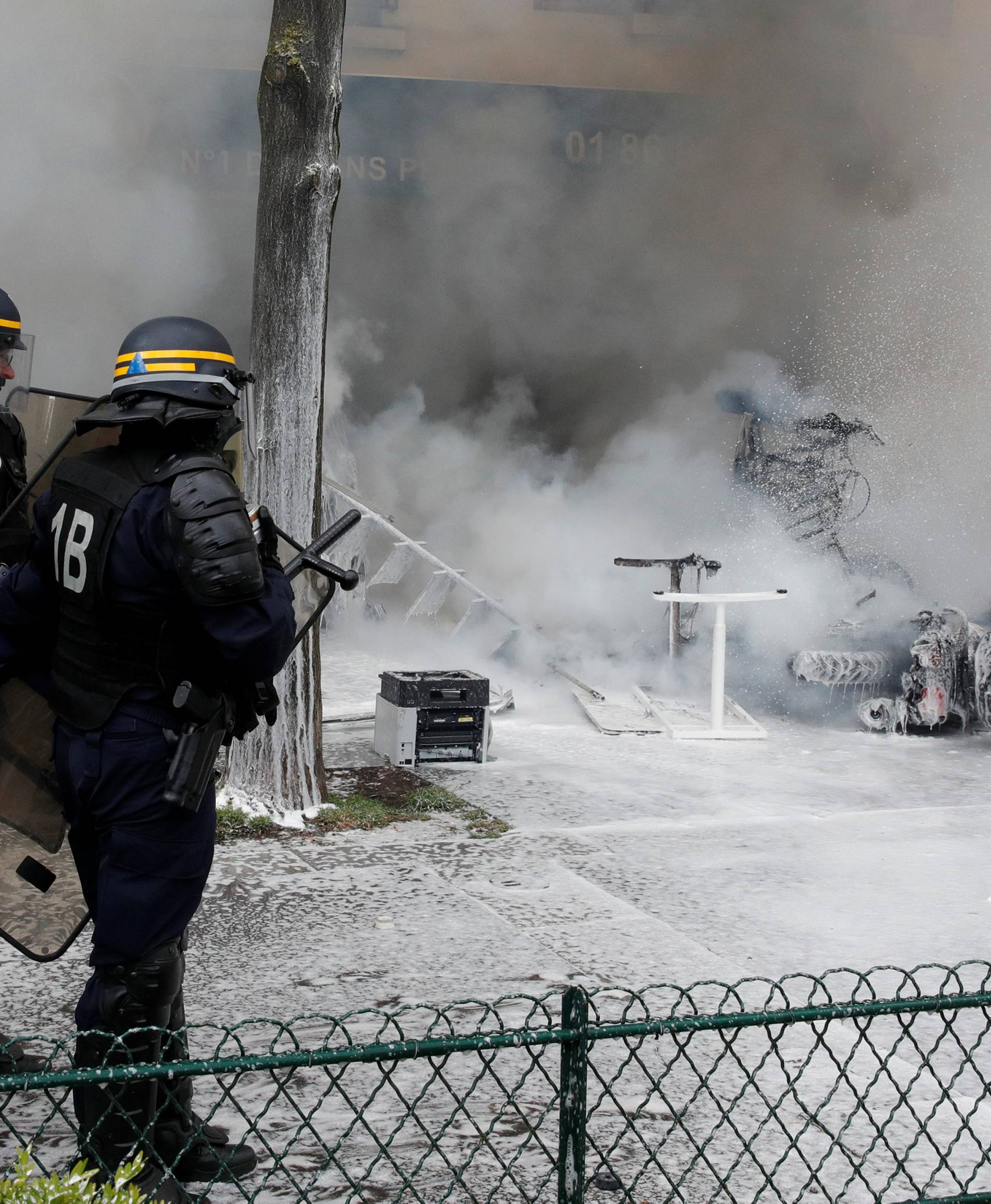 French CRS riot police take position near smoking remains of a vehicle outside a Renault garage during clashes at the May Day labour union march in Paris