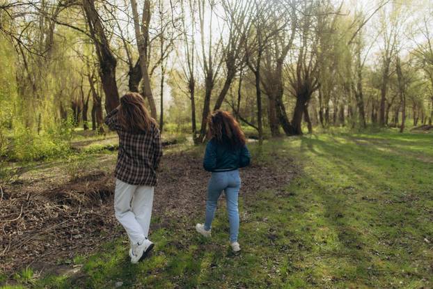 Two Women Walking Together Through a Green Forest in Daylight