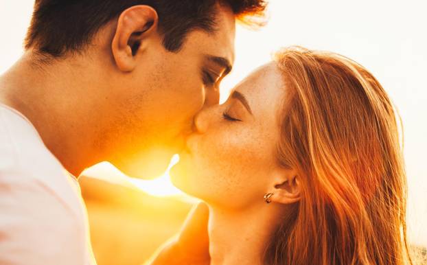 The boy and the girl kissing at their first date in the light of the autumn sun. Portrait on light backdrop. Close up portrait.