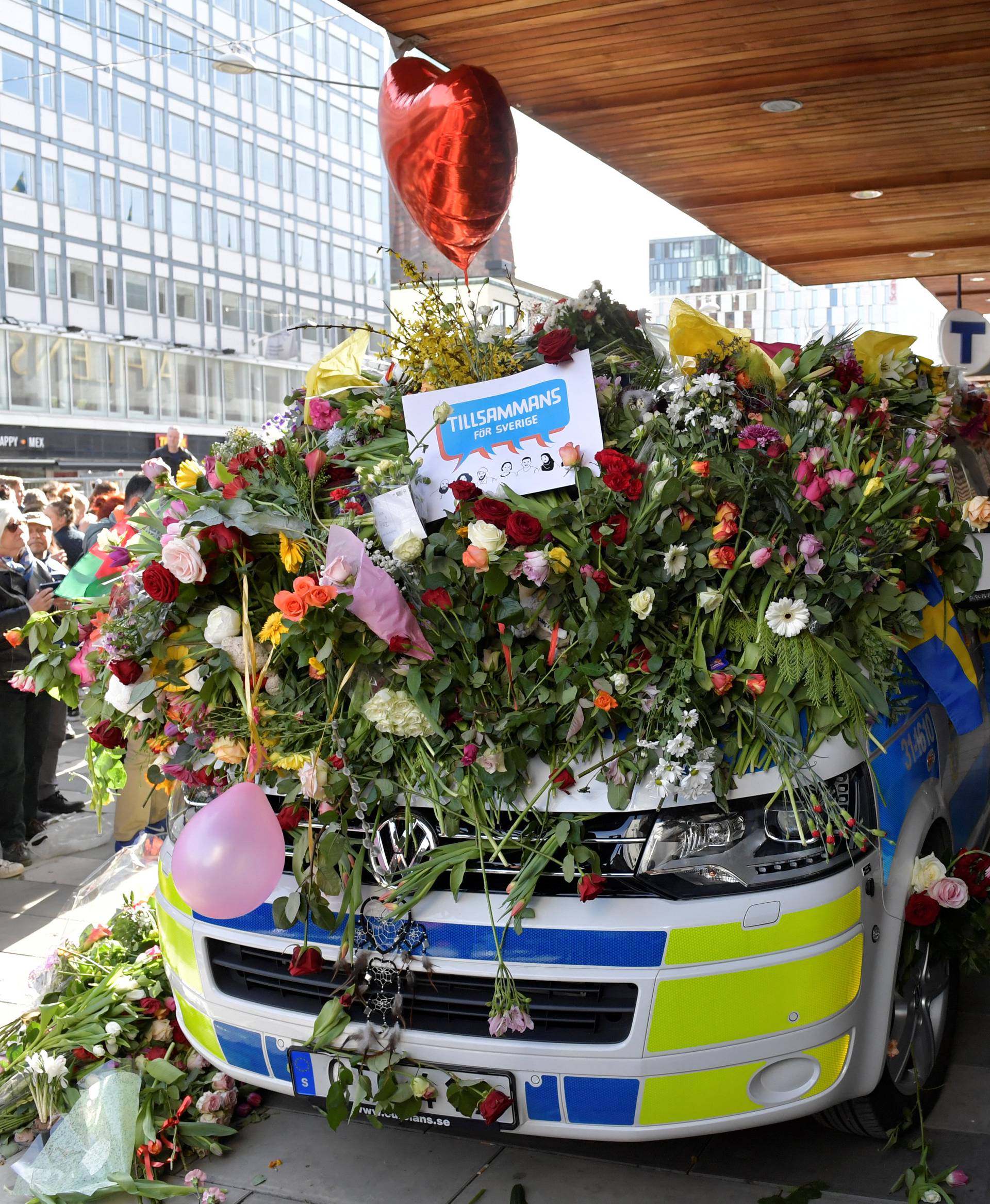 People put flowers on a police vehicle outside Ahlens department store, following Friday's attack, in central Stockholm