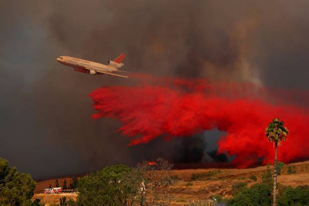 A DC-10 aircraft drops fire retardant on a wind driven wildfire in Orange, California