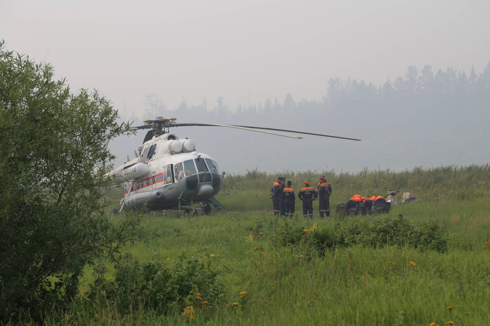 Members of the Russian Emergencies Ministry stand next to a helicopter near the site of a wildfire in Krasnoyarsk region