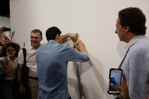 An Art Basel worker attaches a banana with duct-tape in the wall where the artwork 