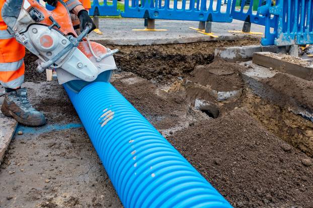 Builder cutting blue plastic duct pipe with petrol concrete saw and a diamond blade during water pipe repair works