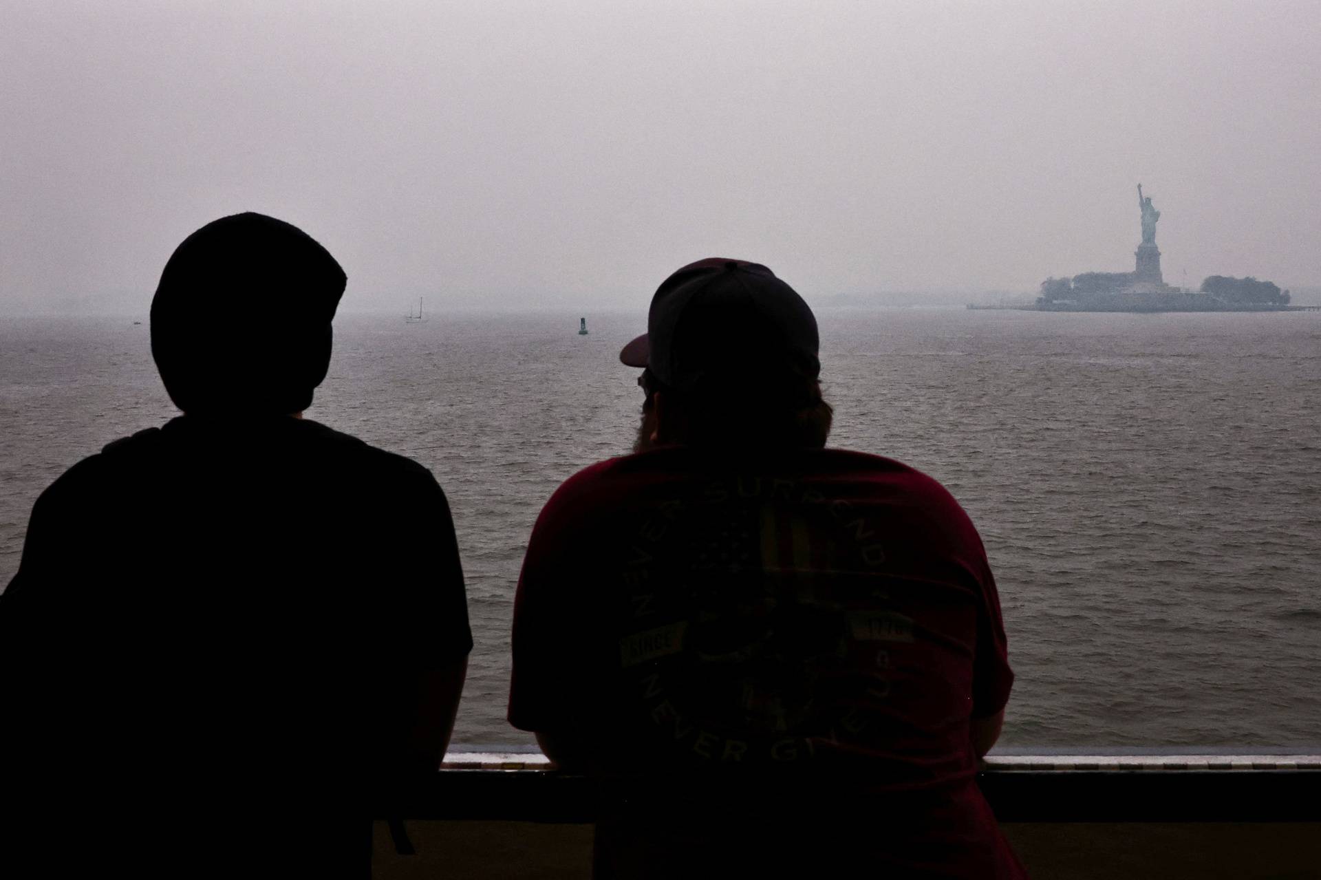 Commuters stand on the Staten Island Ferry while the Statue of Liberty is seen in the background covered by haze and smoke caused by wildfires in Canada, in New York