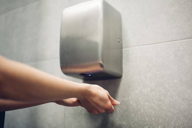 Air dryer in public toilet. Woman drying hands in water closet.