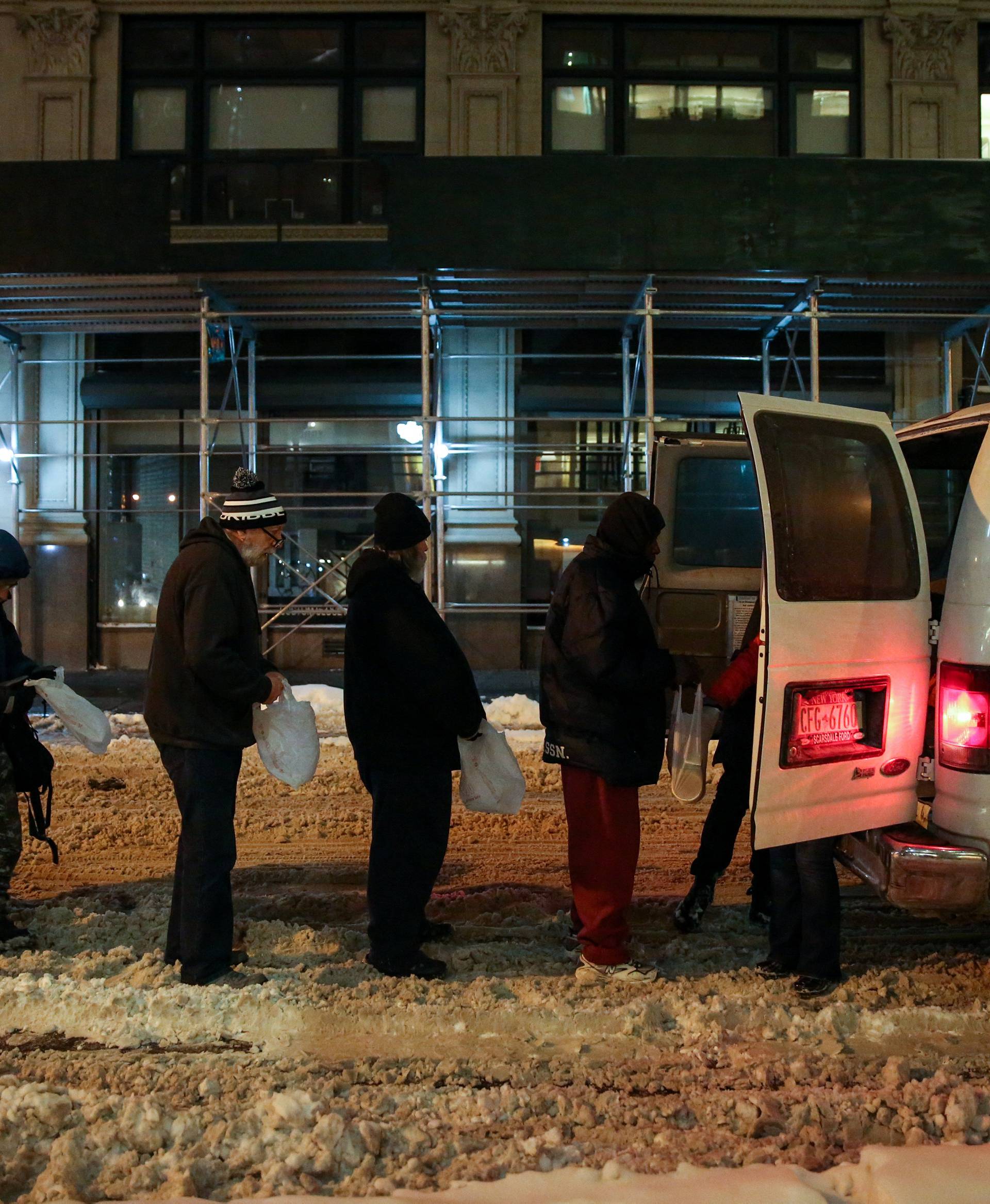 People stand in line as New York City's Coalition for the Homeless delivers food, donated clothing and supplies during winter storm Grayson in New York