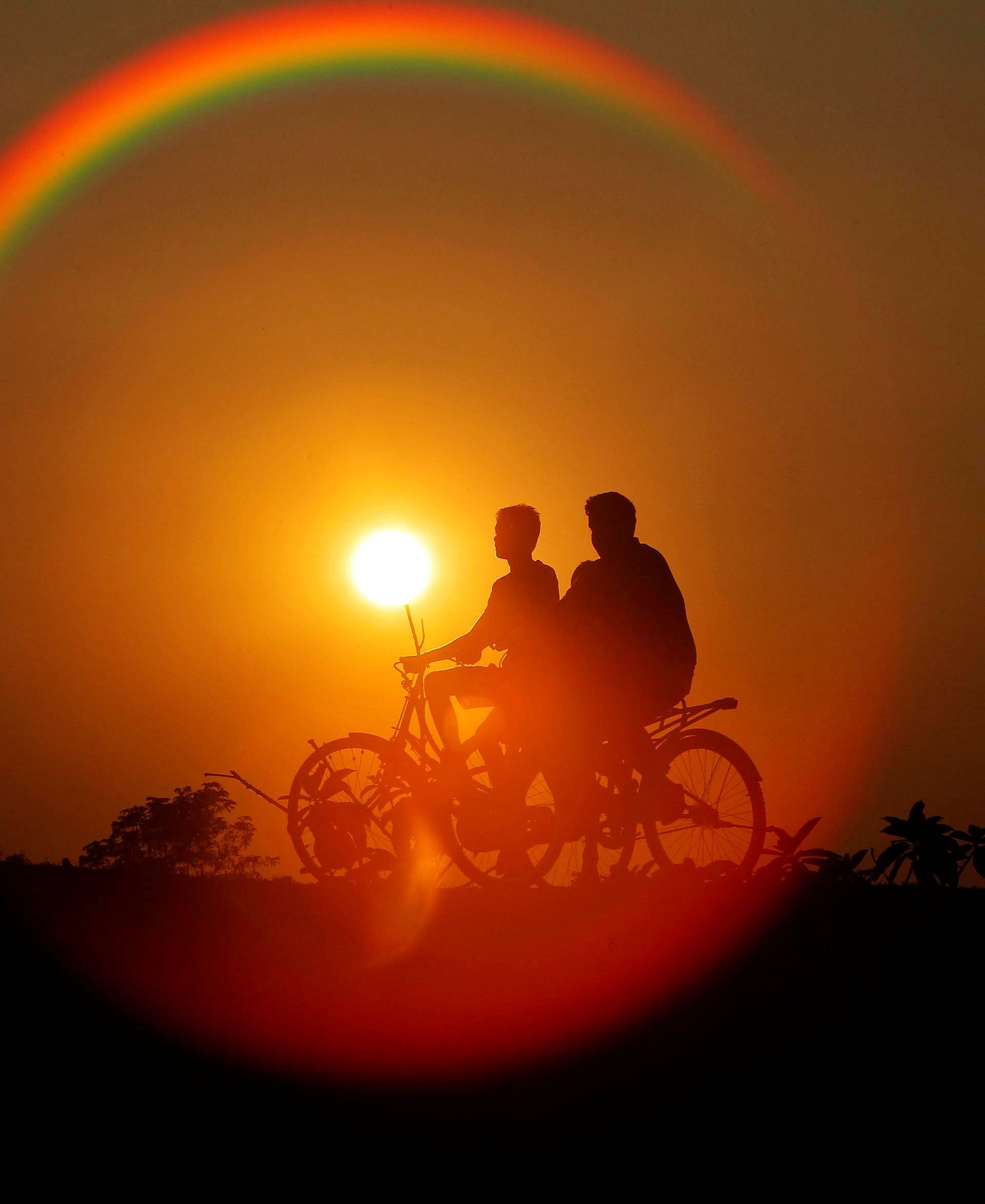 Boys are silhouetted against the setting sun as they ride bicycles on the outskirts of Agartala