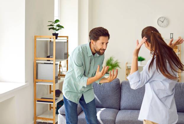 Young couple man and woman standing at home and arguing shouting in quarrel.