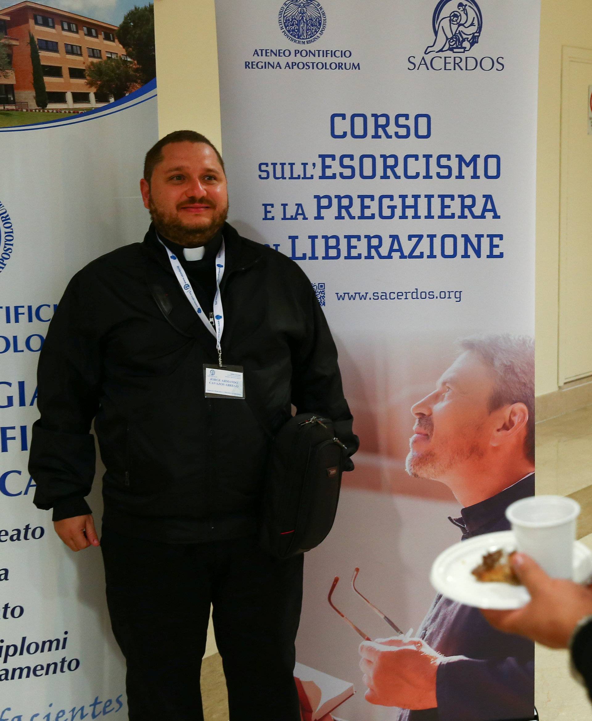 A priest poses for a picture next to a banner advertising a course for aspiring exorcists in Rome