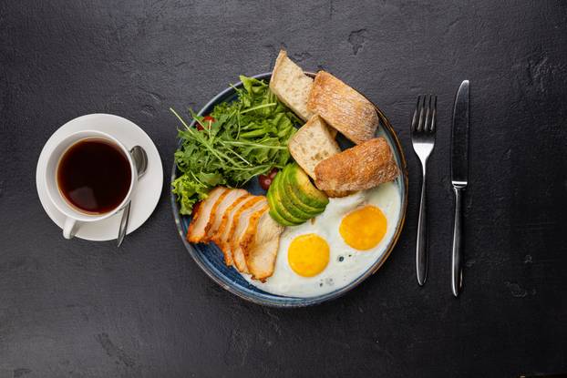 Healthy breakfast plate with eggs, avocado, chicken, greens, and ciabatta bread