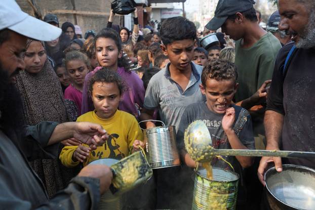 Palestinians gather to receive meals cooked by a charity kitchen, in Deir Al-Balah, central Gaza Strip