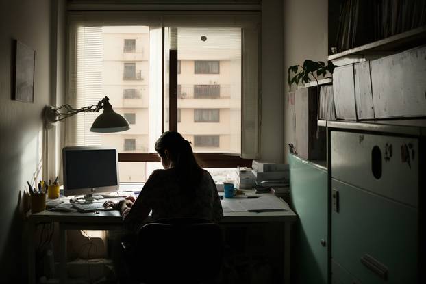 A person sits at a computer in an indoor office, surrounded by m