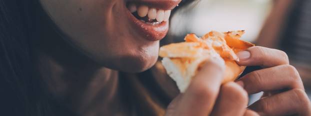 Funny brunette girl in yellow sweater eating pizza at restaurant