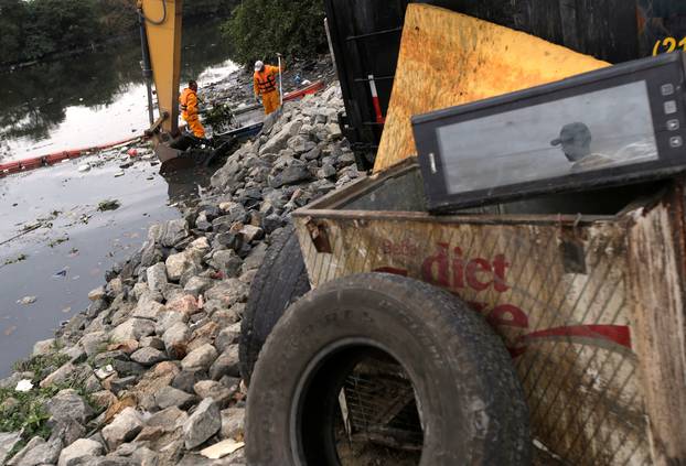 Men work cleaning up the garbage next to an ecobarrier at Meriti River which flows into Guanabara Bay, in Duque de Caxias, near Rio de Janeiro