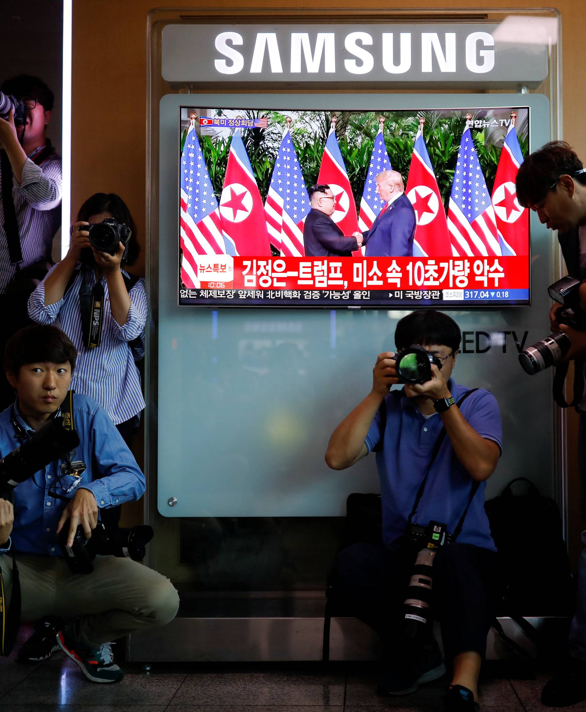 Photographers surround a TV broadcasting a news report on summit between the U.S. and North Korea, in Seoul