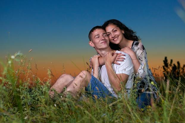 romantic couple sit on grass at sunset on outdoor, beautiful landscape and dark night sky sky, love concept, young adult people