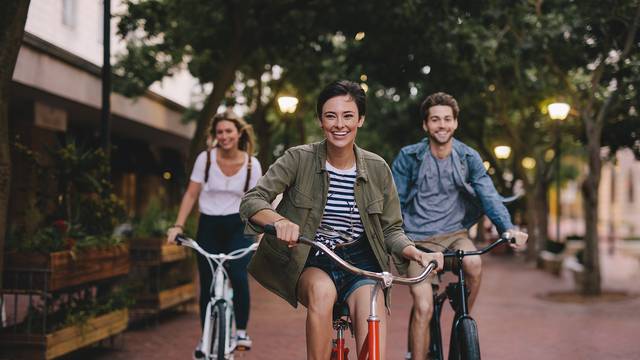 Three,Young,People,Cycling,Down,The,Street.,Male,And,Female