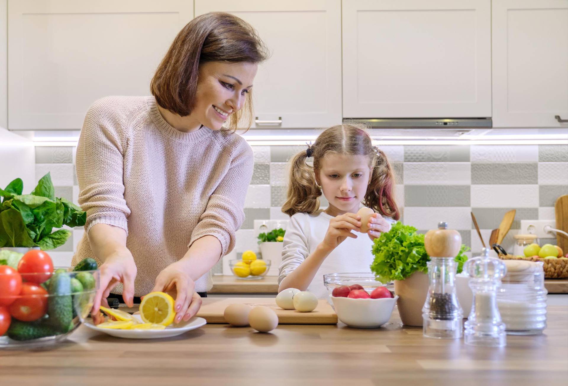 Smiling mother and daughter 8, 9 years old cooking together in kitchen vegetable salad. Healthy home food, communication parent and child.