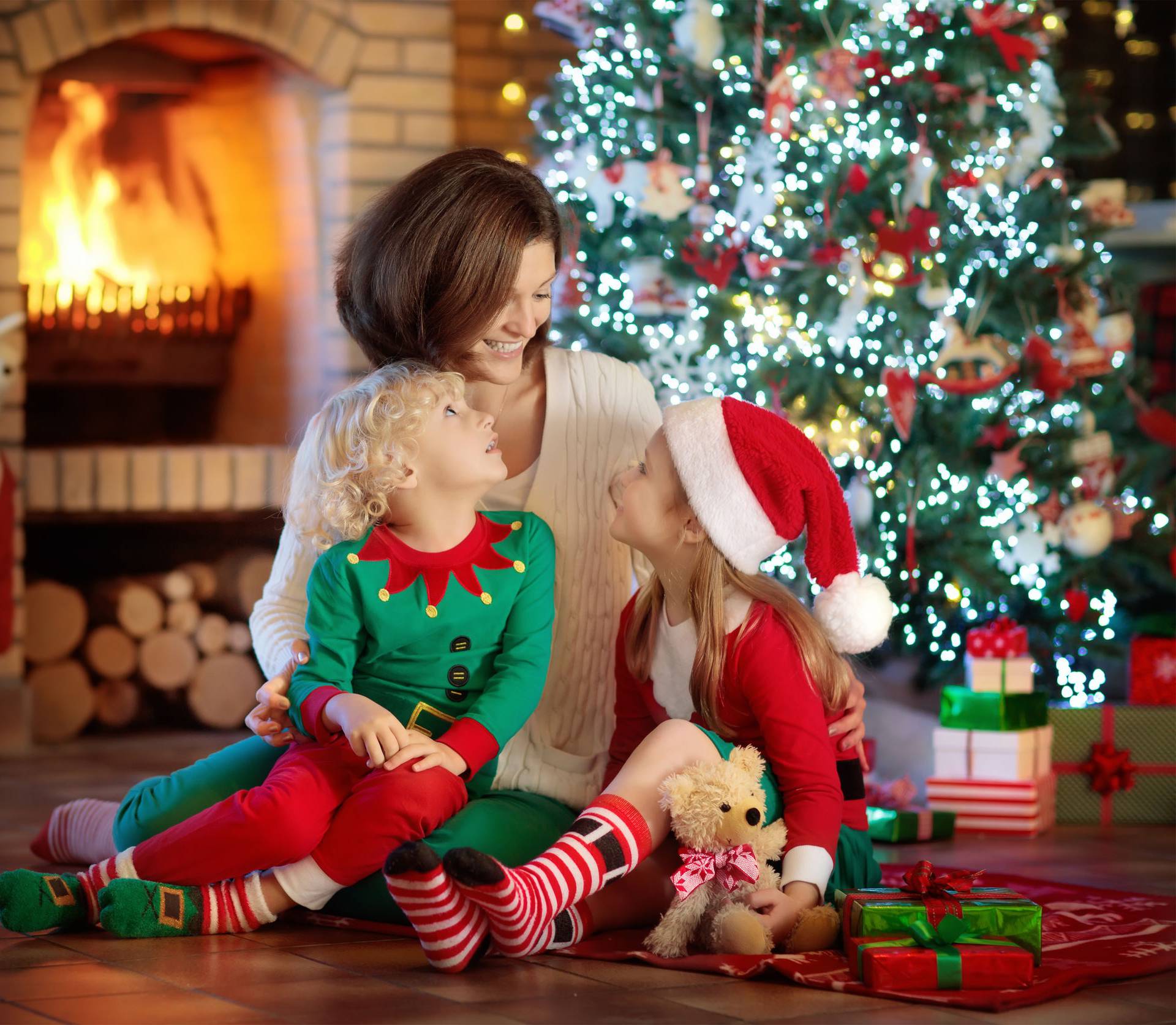 Family with kids at Christmas tree and fireplace. Mother and chi