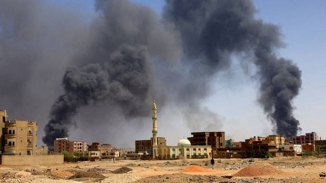 FILE PHOTO: FILE PHOTO: Man walks while smoke rises above buildings after aerial bombardment in Khartoum North