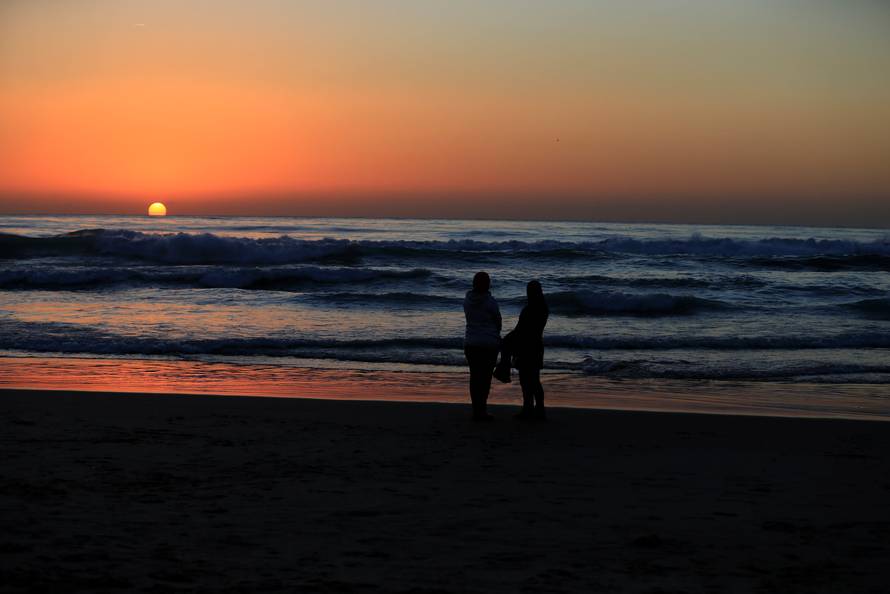Two women watch the sunset over the Mediterranean sea on a cold day at a public beach in Beirut