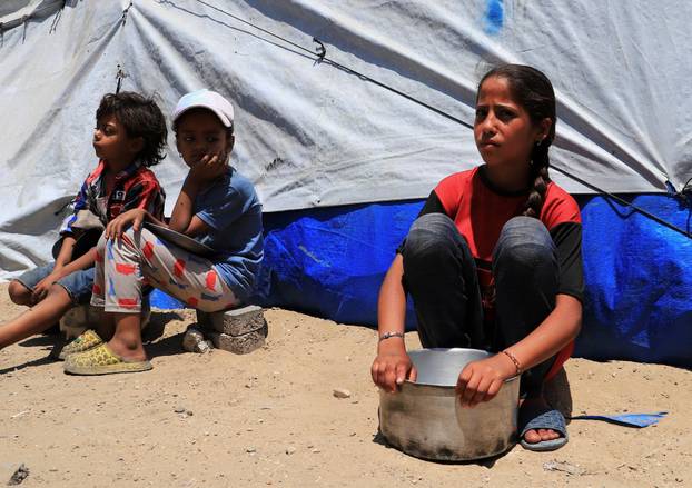 Displaced Palestinian children, one with an empty pot, sit while waiting to receive food from a charity kitchen, in Gaza City