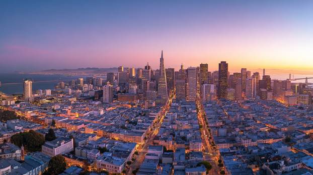 San francisco skyline shining at dusk with bay bridge in background